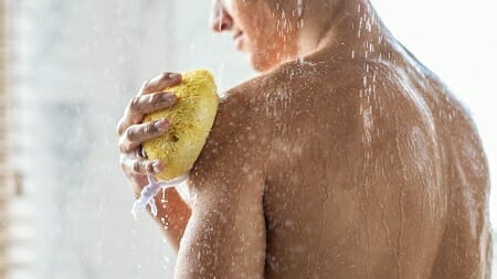 Man cleansing himself in shower using yellow sponge